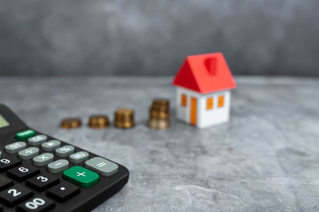 A calculator with mini model house and coins in the concept of budgeting