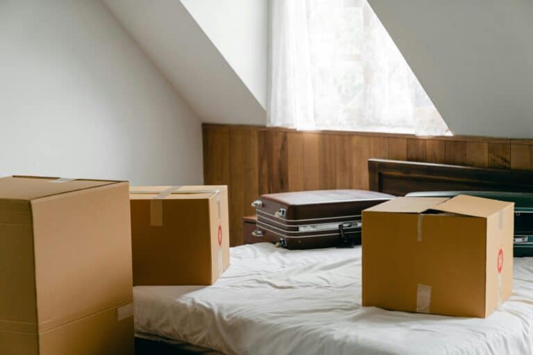 Cardboard boxes and suitcases on top of the bed in the concept of moving to Enfield.