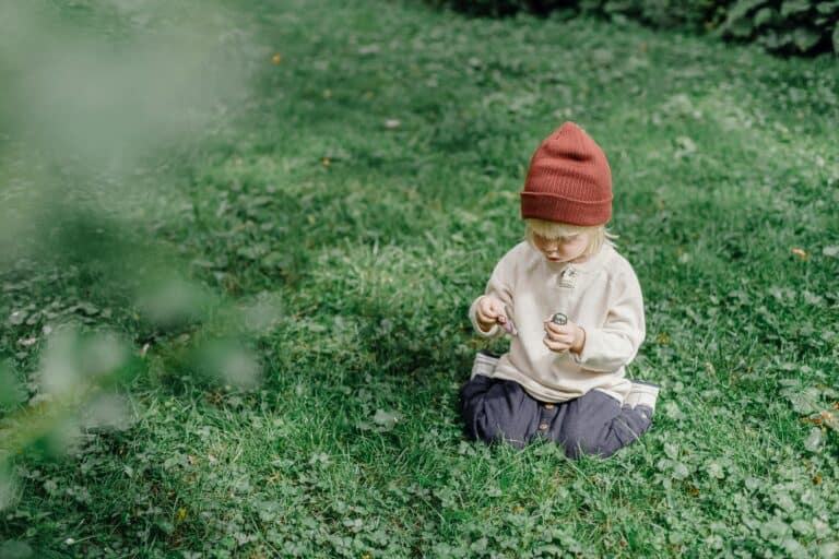 A young child sitting on the lawn in the concept 'best parks and green spaces in Enfield'.